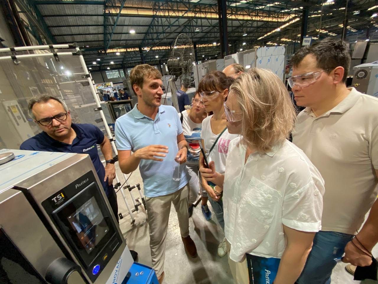Um grupo de pessoas está em volta de uma máquina em um armazém.