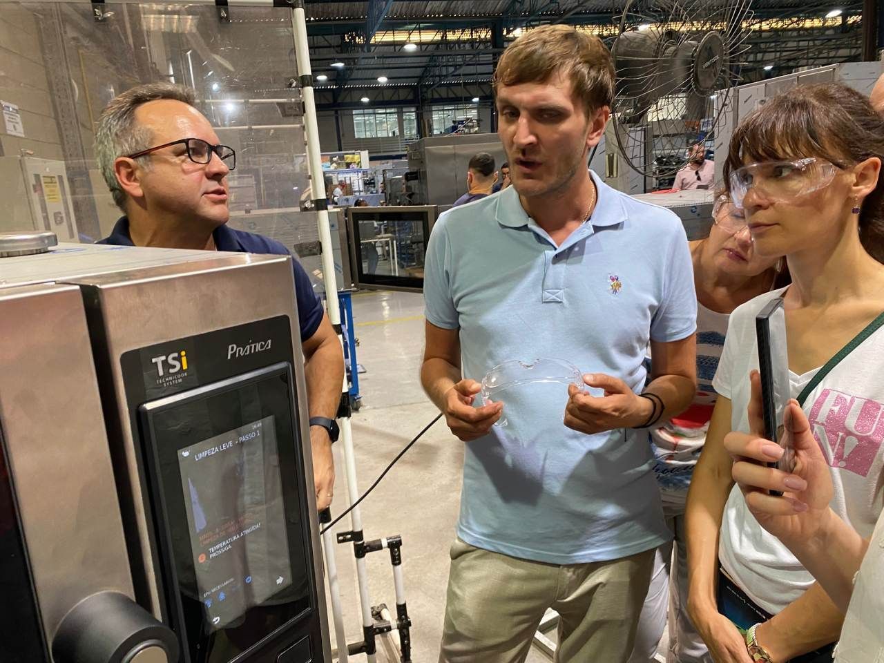 Um grupo de pessoas está em volta de uma máquina em uma fábrica.