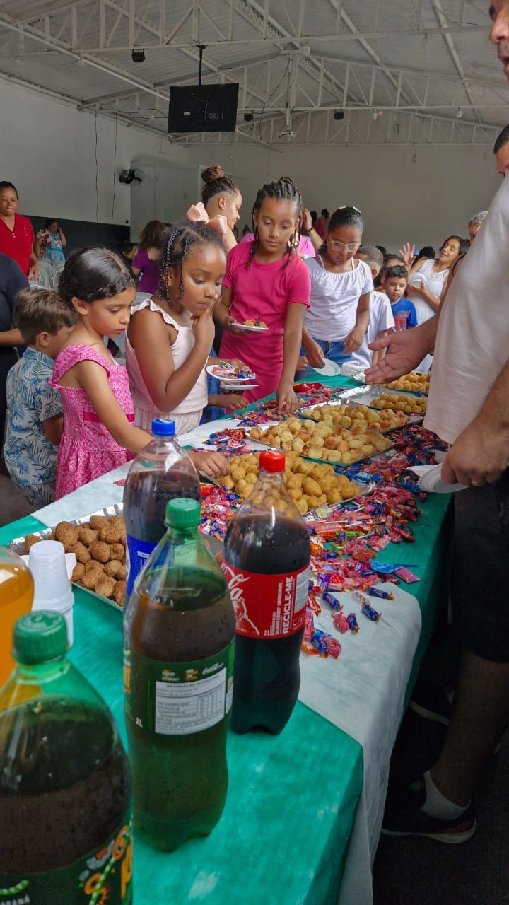 Um grupo de crianças está em pé ao redor de uma mesa com comida e bebidas.