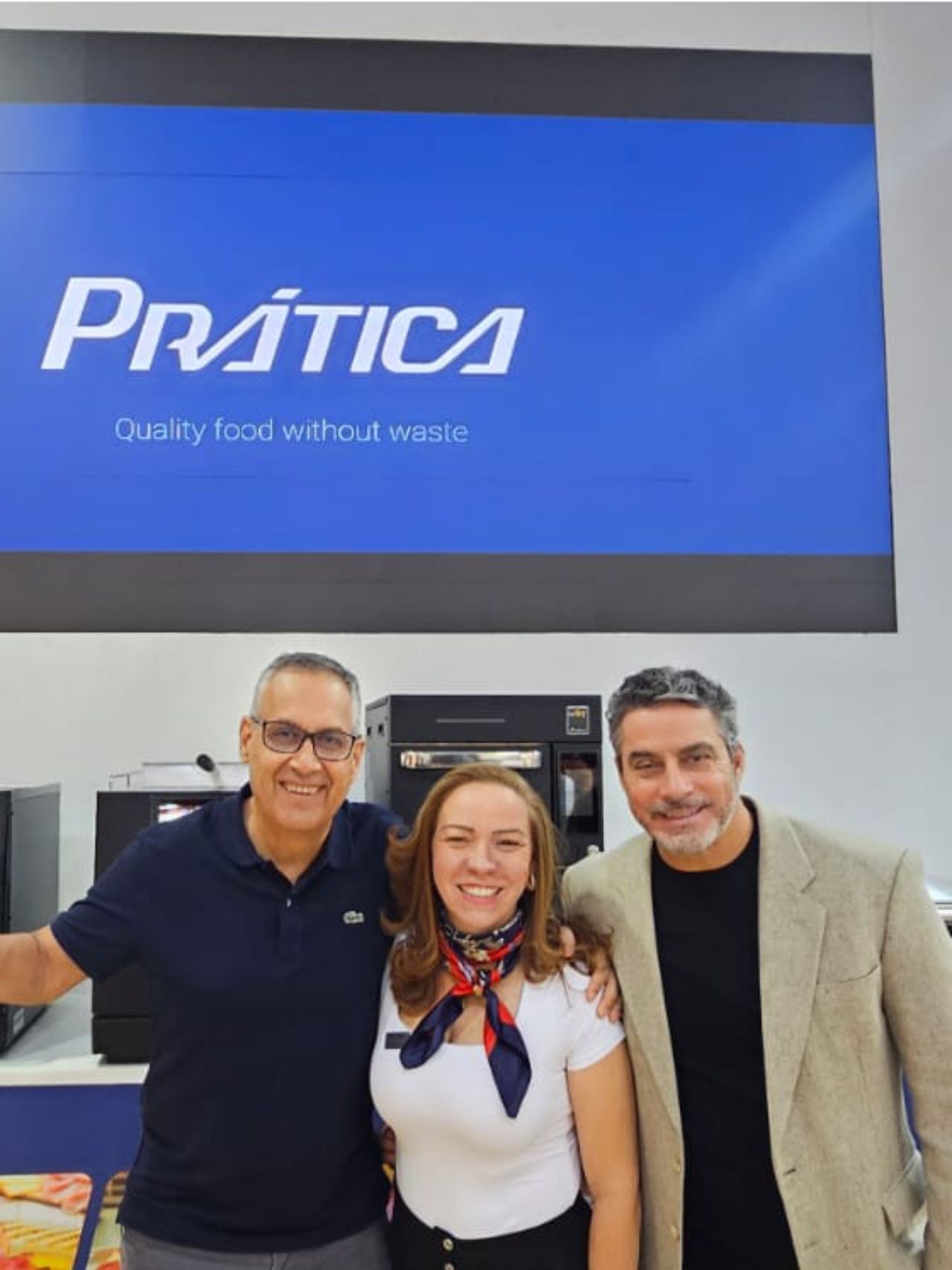 Três pessoas sorrindo em frente a uma placa azul que diz
