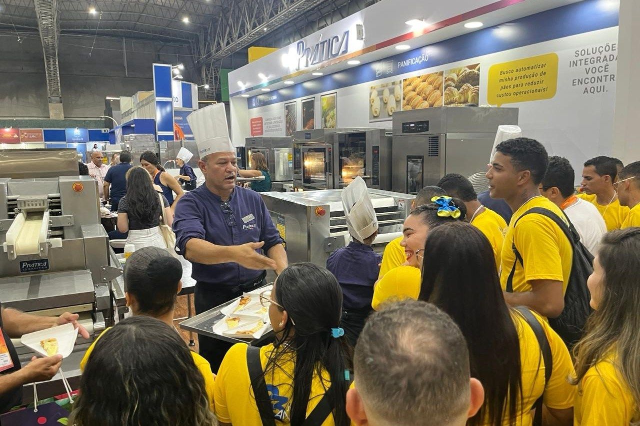 Um homem com chapéu de chef está conversando com um grupo de pessoas.