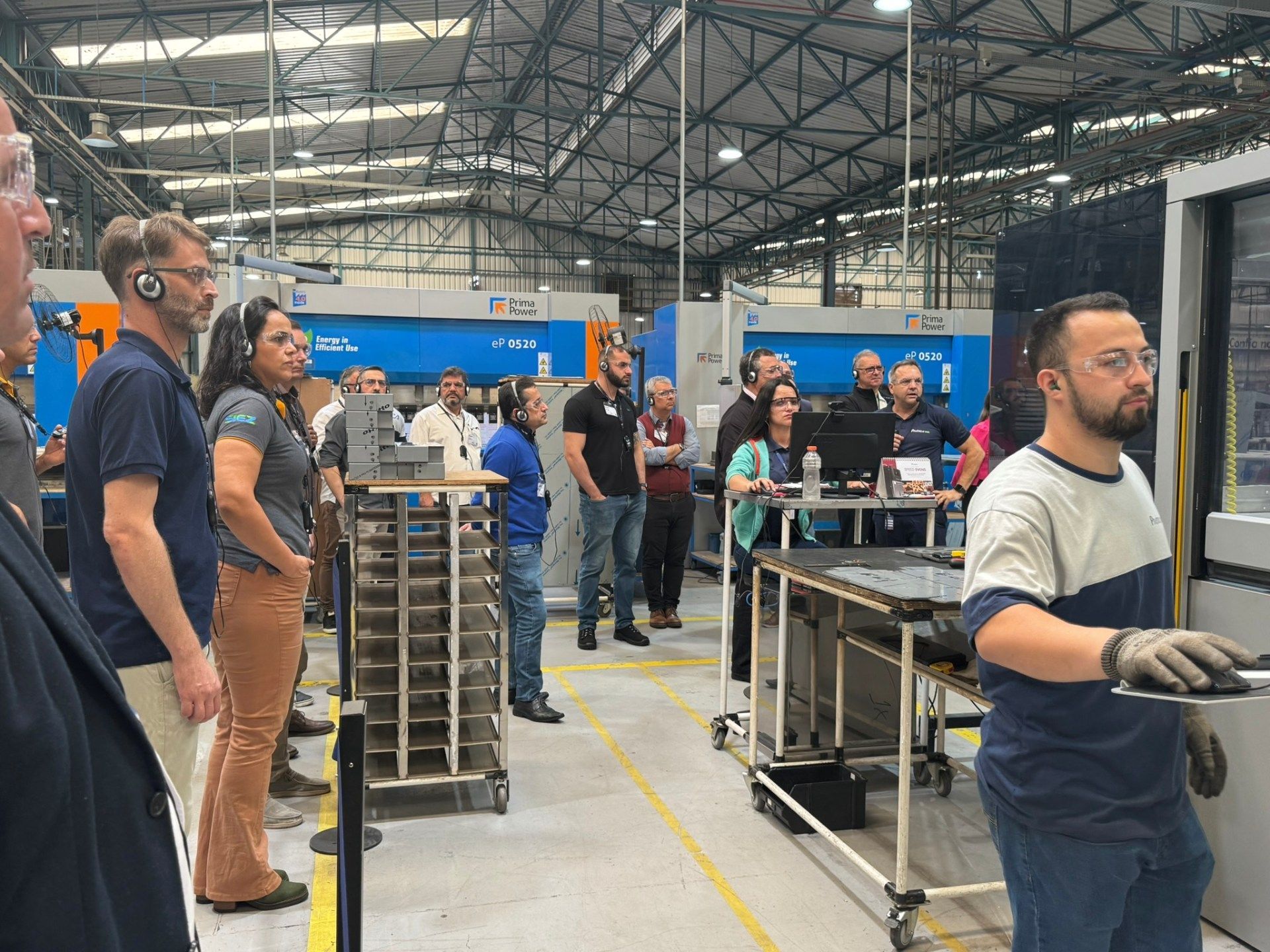 Um grupo de pessoas está em uma fábrica olhando para uma máquina.