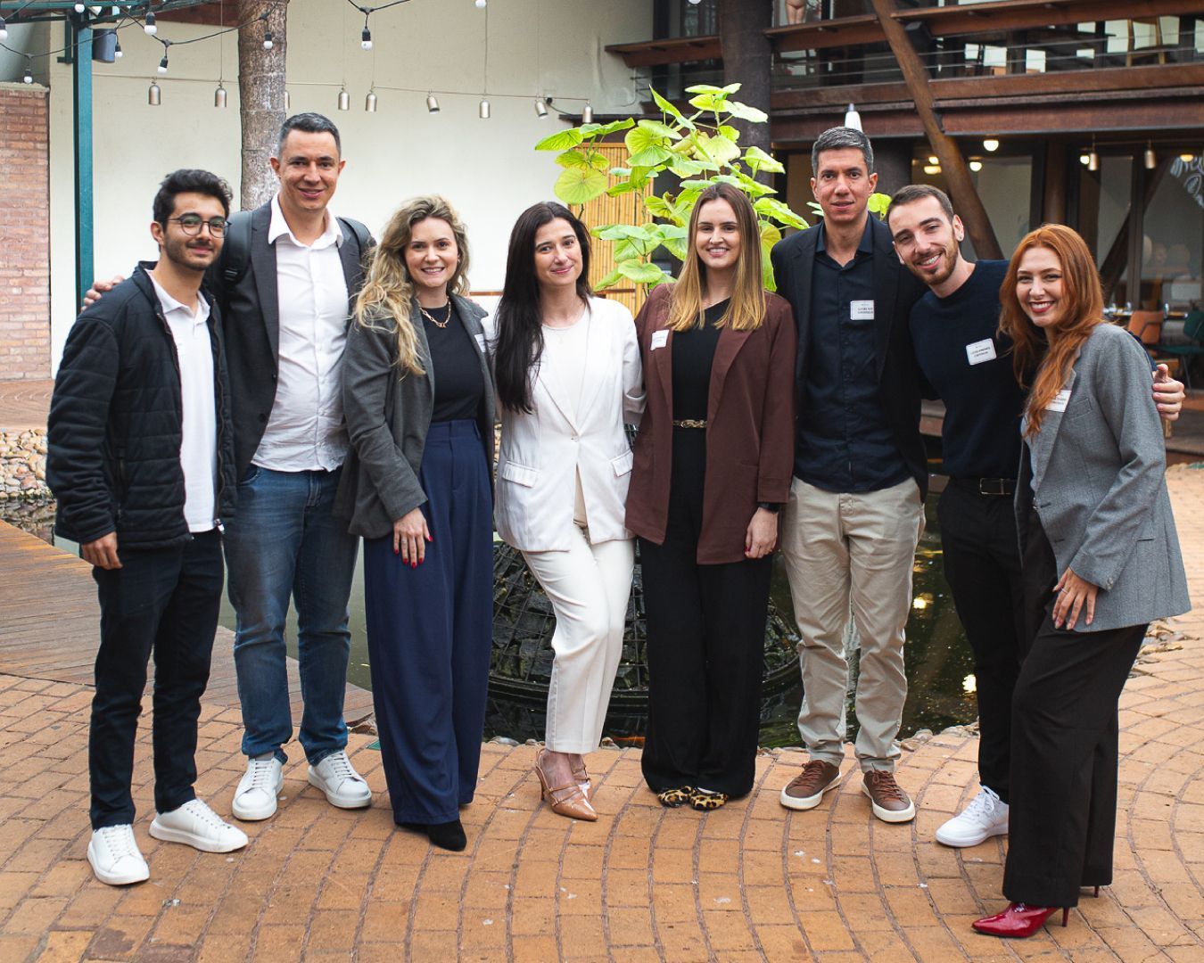 Grupo de nove pessoas sorrindo, posando ao ar livre em um pátio de tijolos.