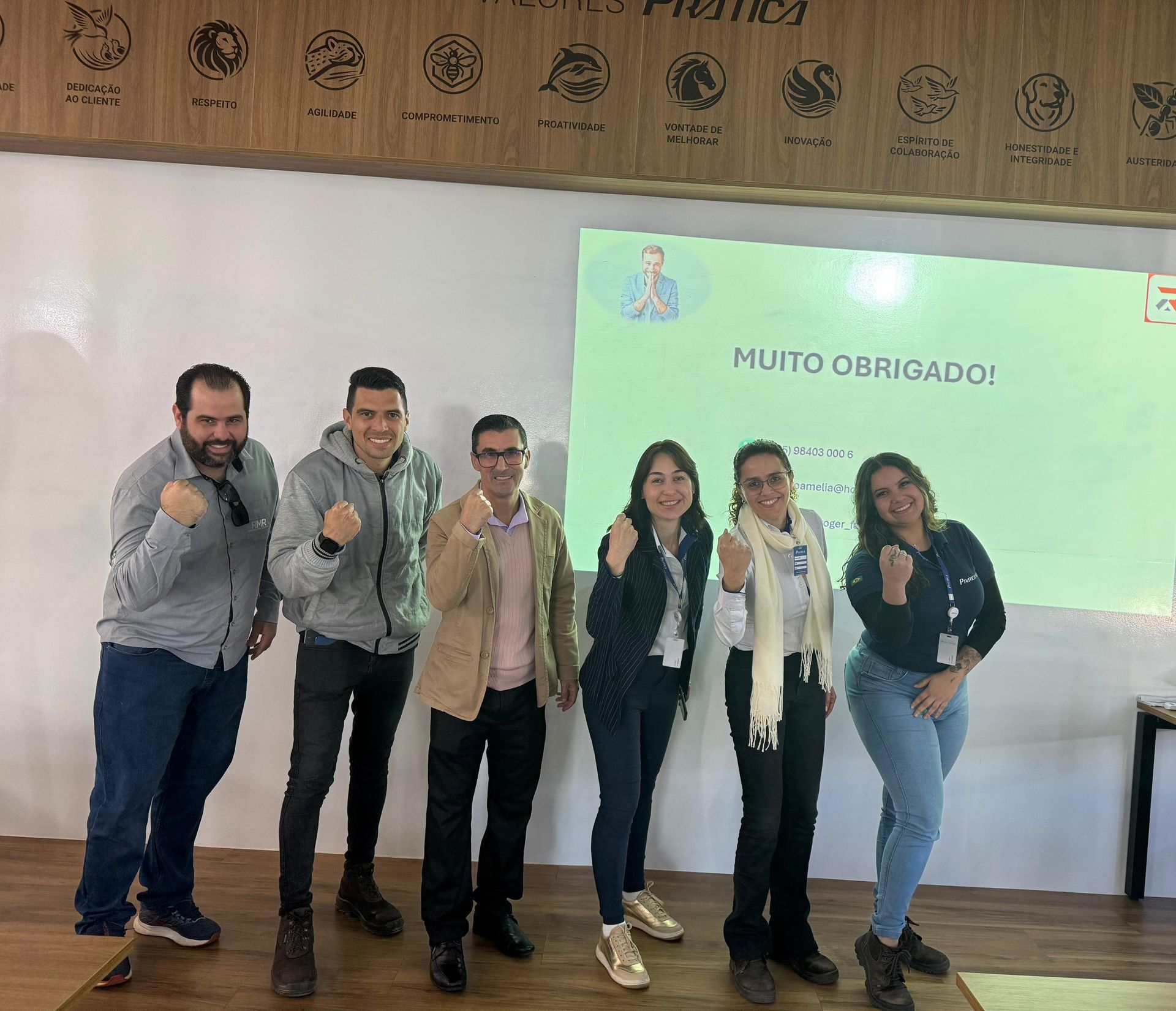 Um grupo de pessoas está posando para uma foto em frente a uma tela grande.