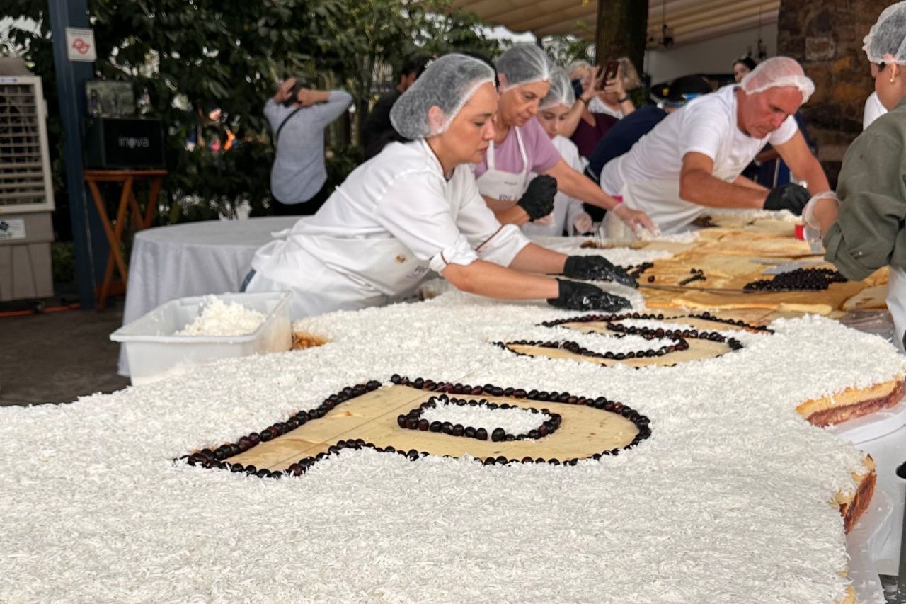Pessoas decorando um bolo grande com glacê branco e as letras 