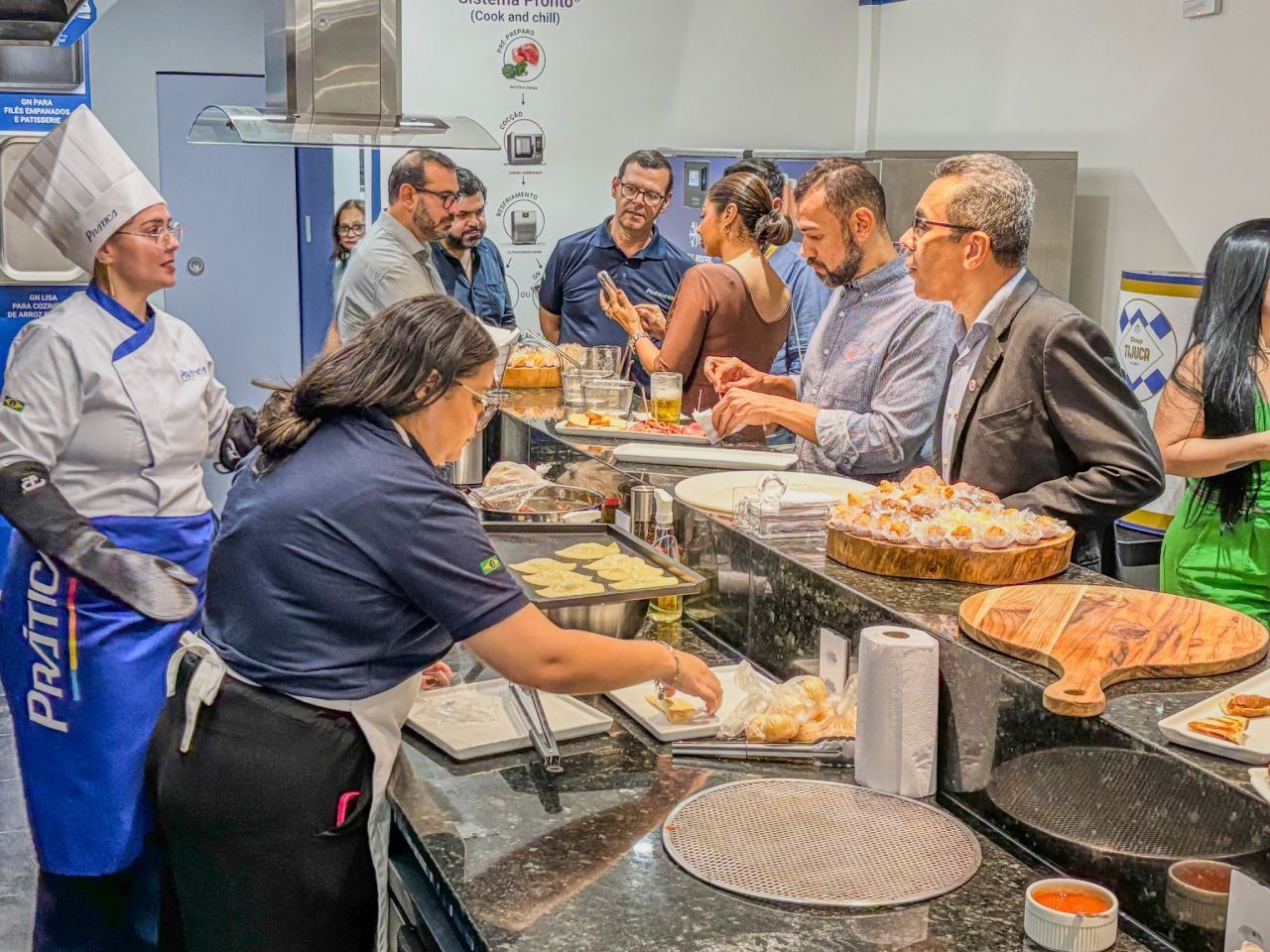 Chefs e convidados em uma cozinha comercial; um chef está montando os pratos.