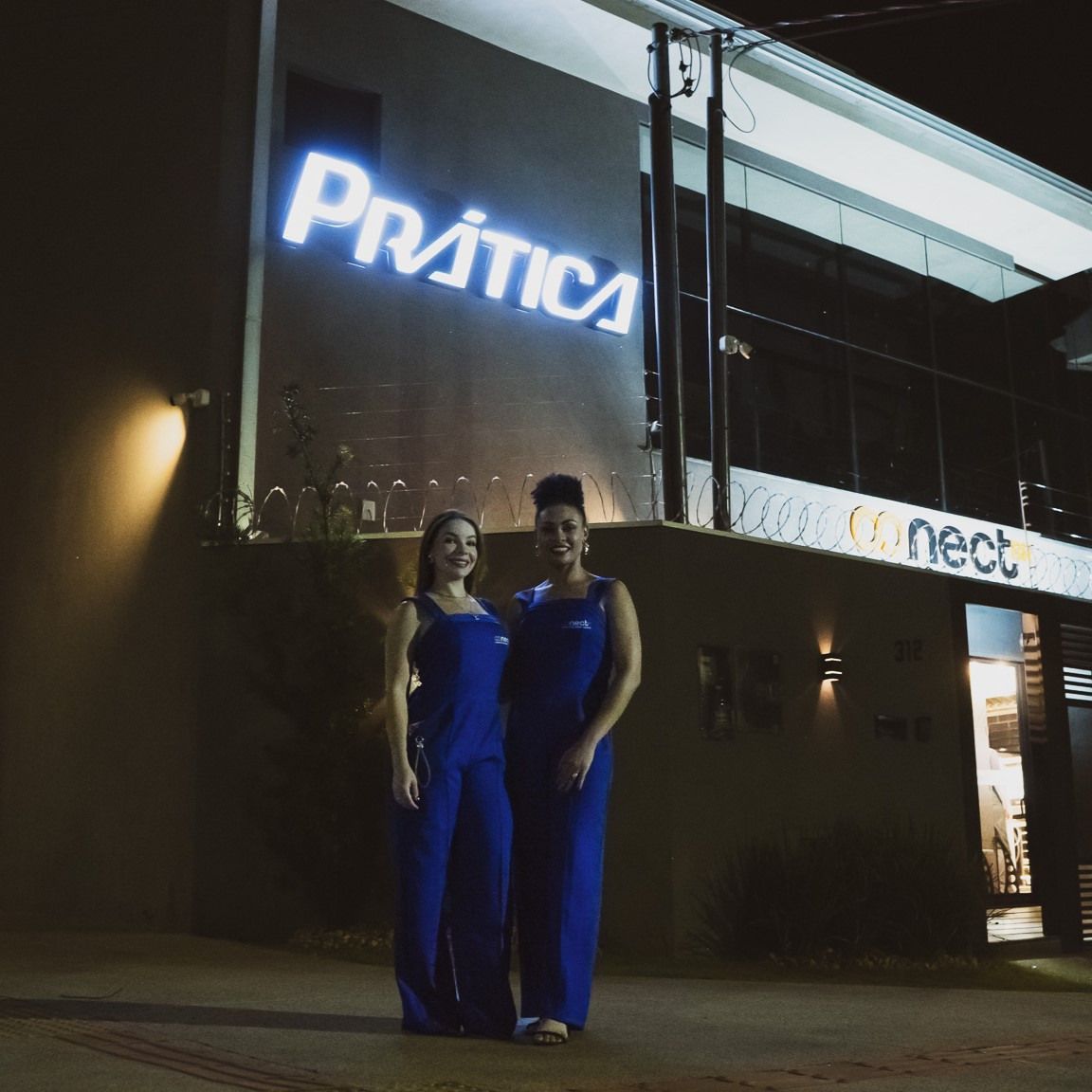 Duas mulheres em pé em frente a um prédio que diz prática