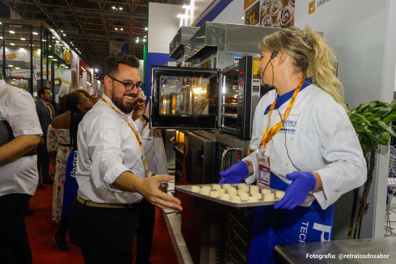 Um homem e uma mulher estão segurando uma bandeja de biscoitos em frente ao forno.
