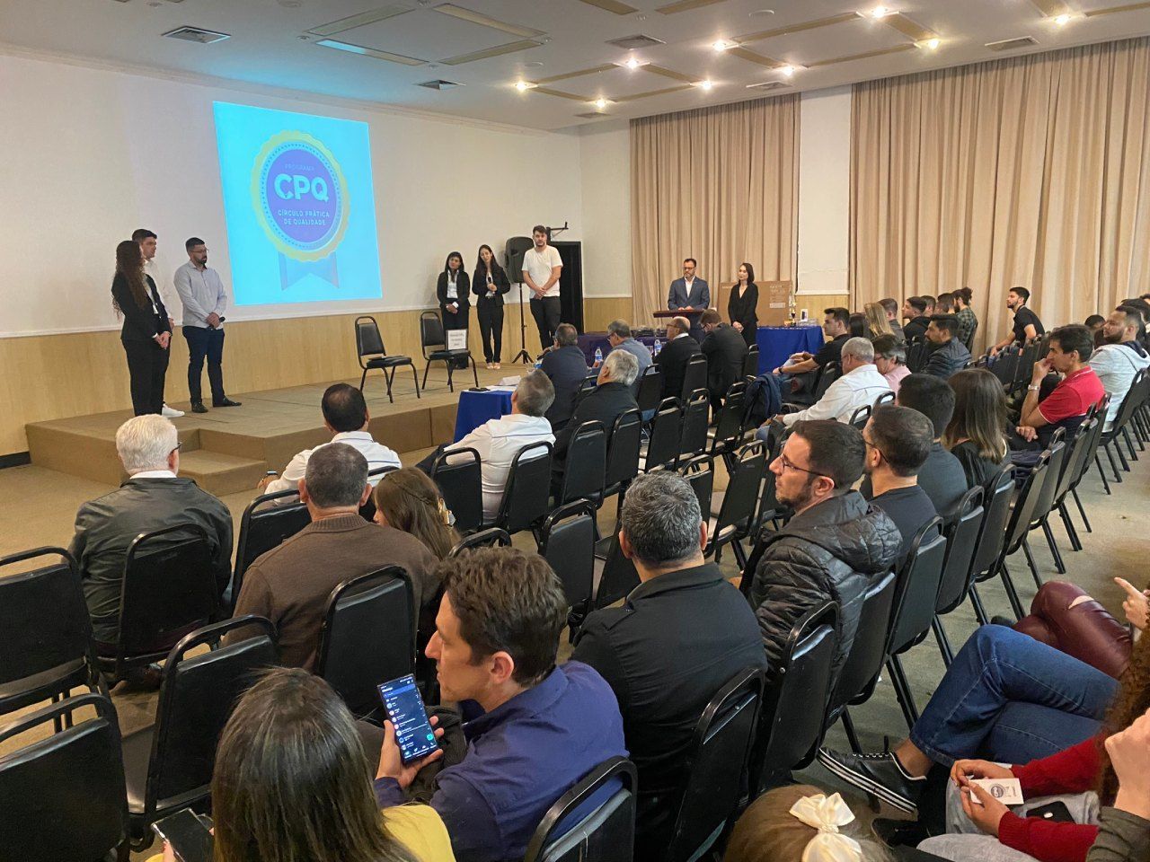 Um grande grupo de pessoas está sentado em cadeiras em uma sala de conferências.