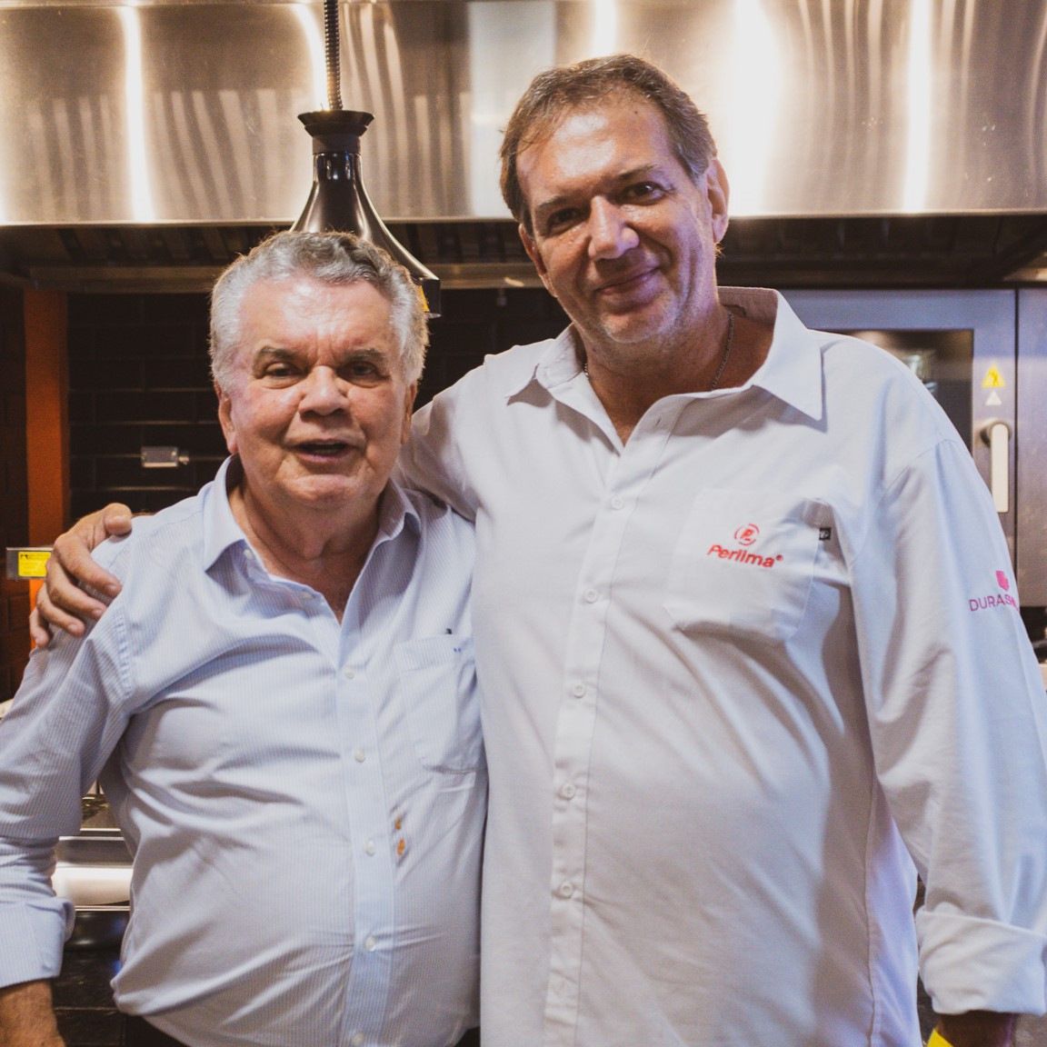Dois homens posando para uma foto, um deles vestindo uma camisa que diz 