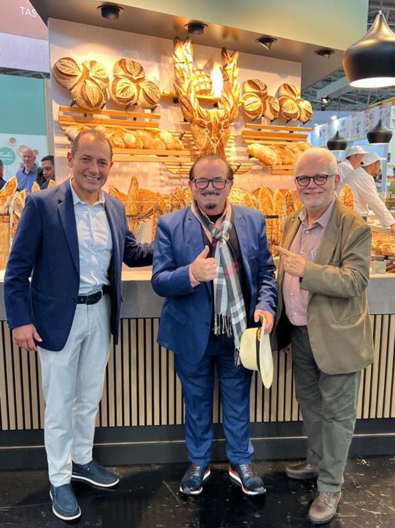 Três homens estão posando para uma foto em frente a uma vitrine de pães.