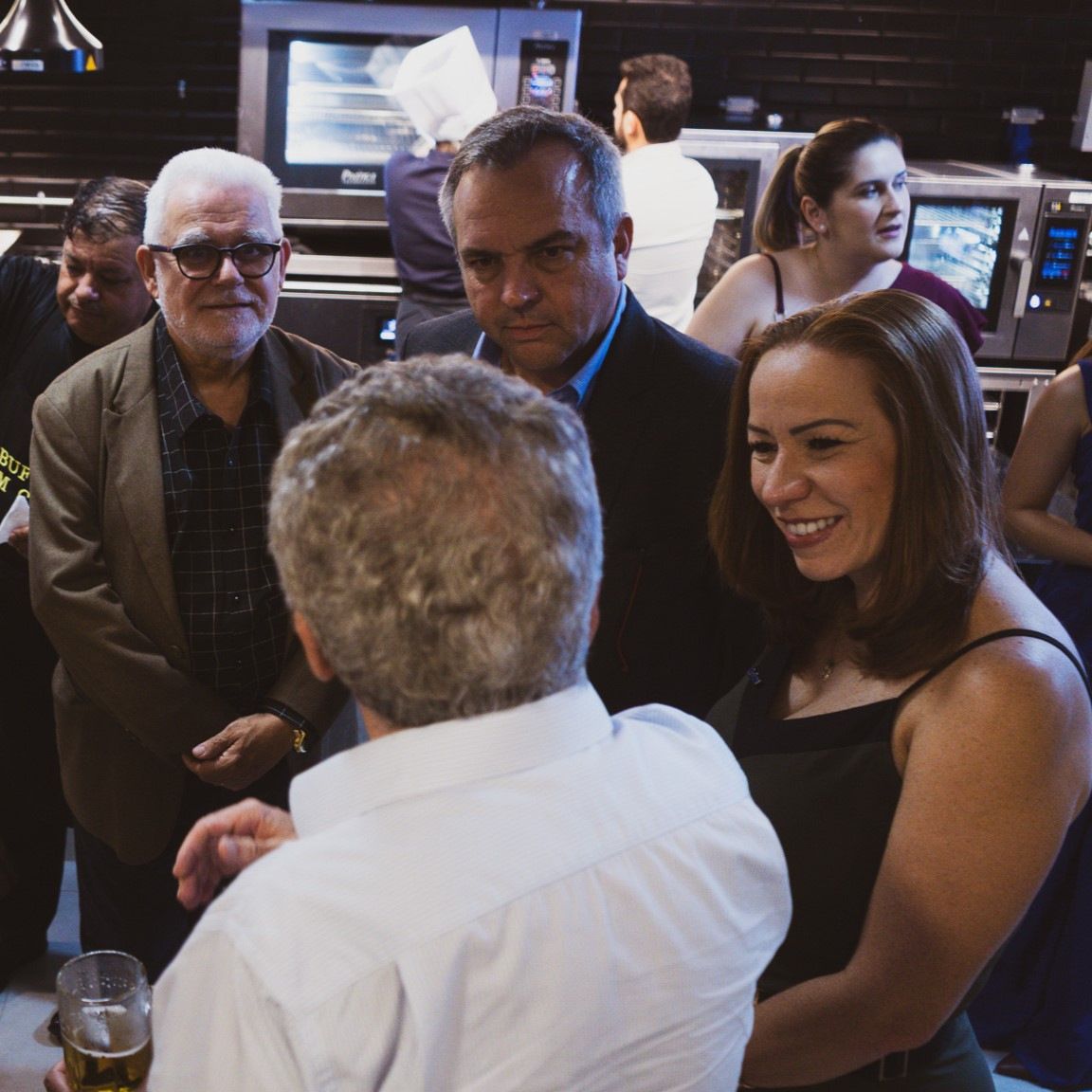 Um grupo de pessoas está em volta de um homem segurando um copo de cerveja
