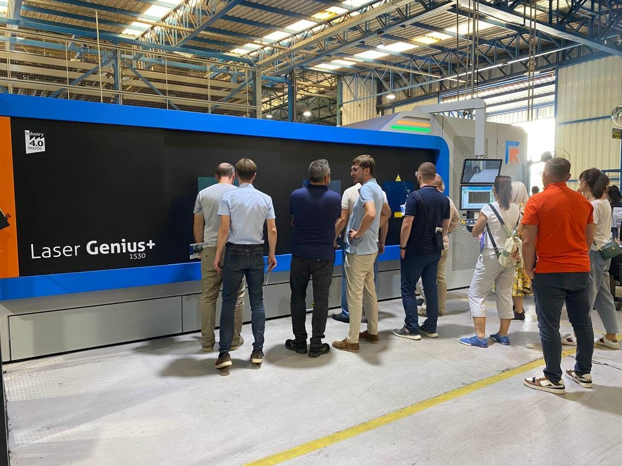 Um grupo de pessoas está em frente a uma máquina em uma fábrica.