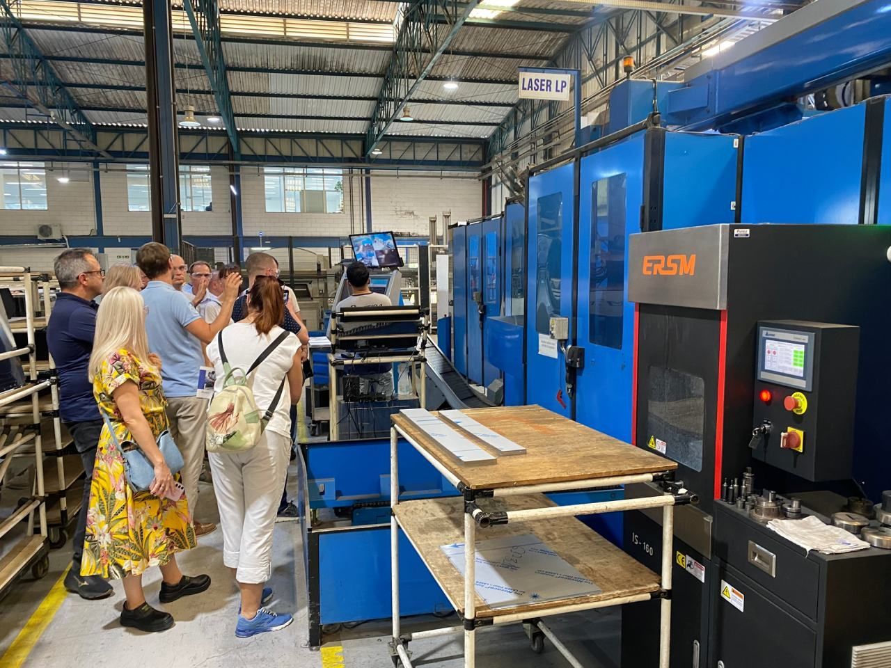 Um grupo de pessoas está em uma fábrica olhando para uma máquina.
