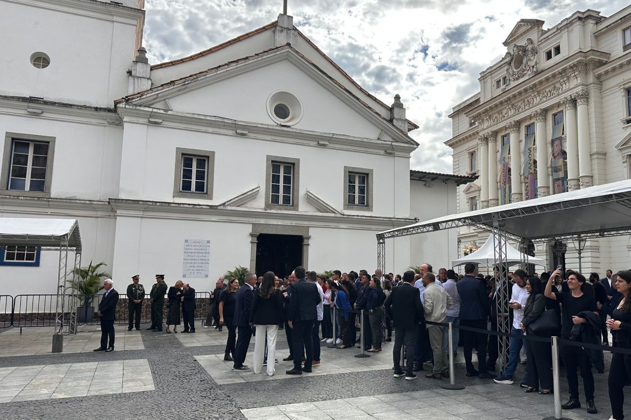 Pessoas fazem fila do lado de fora de uma igreja branca, onde uma grande multidão está reunida.