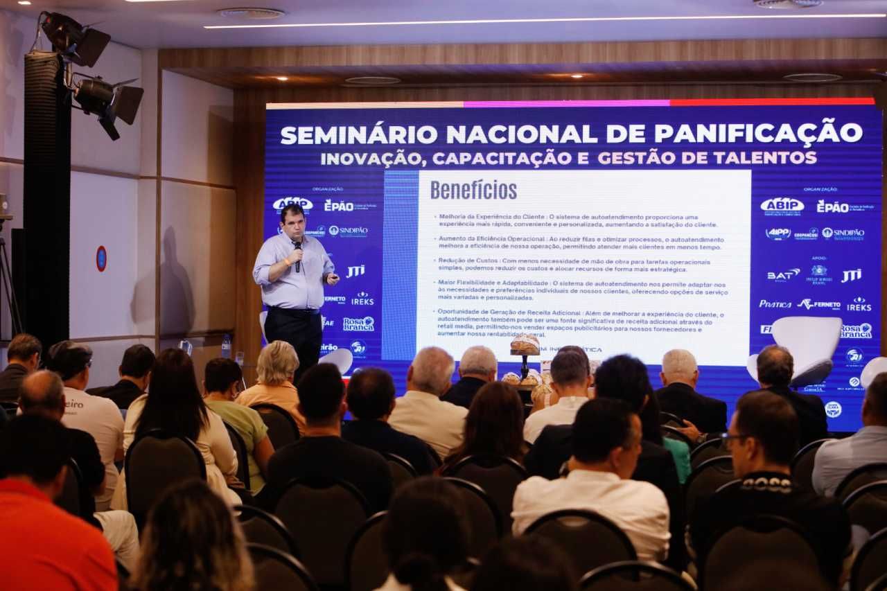 Um homem está fazendo uma apresentação em frente a uma tela grande que diz seminário nacional de panificação