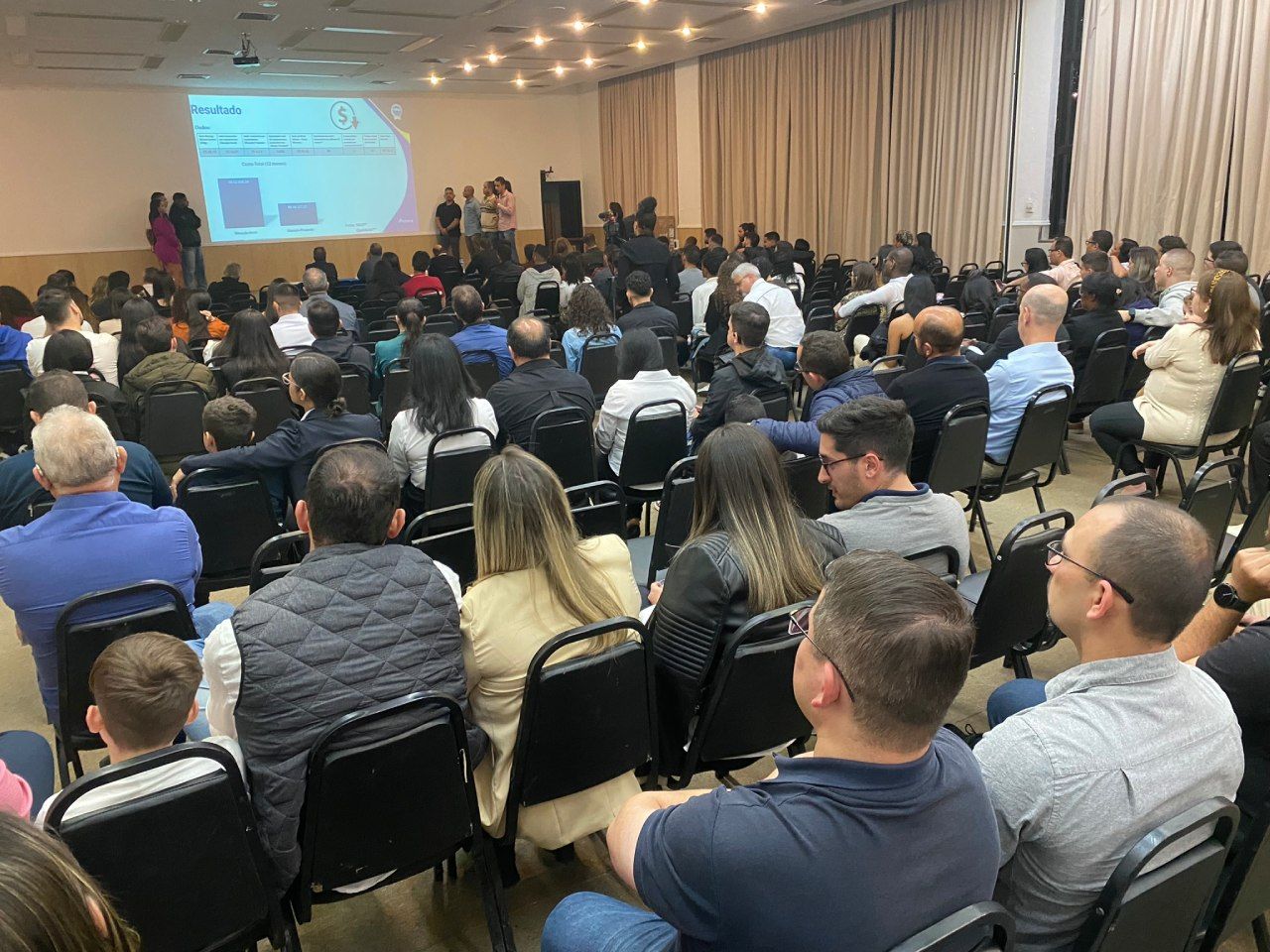 Um grande grupo de pessoas está sentado em cadeiras em uma sala de conferências.