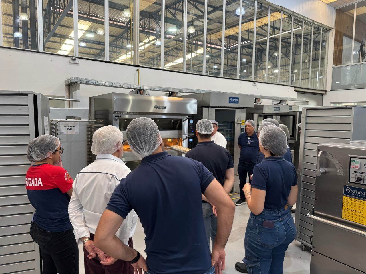 Um grupo de pessoas está em uma cozinha olhando para uma máquina.