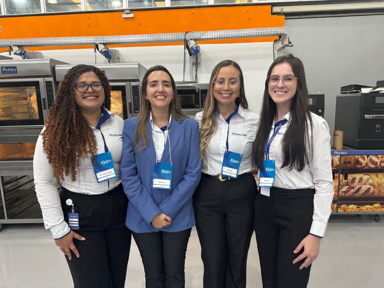 Quatro mulheres em uniformes brancos e pretos, posando em uma padaria.