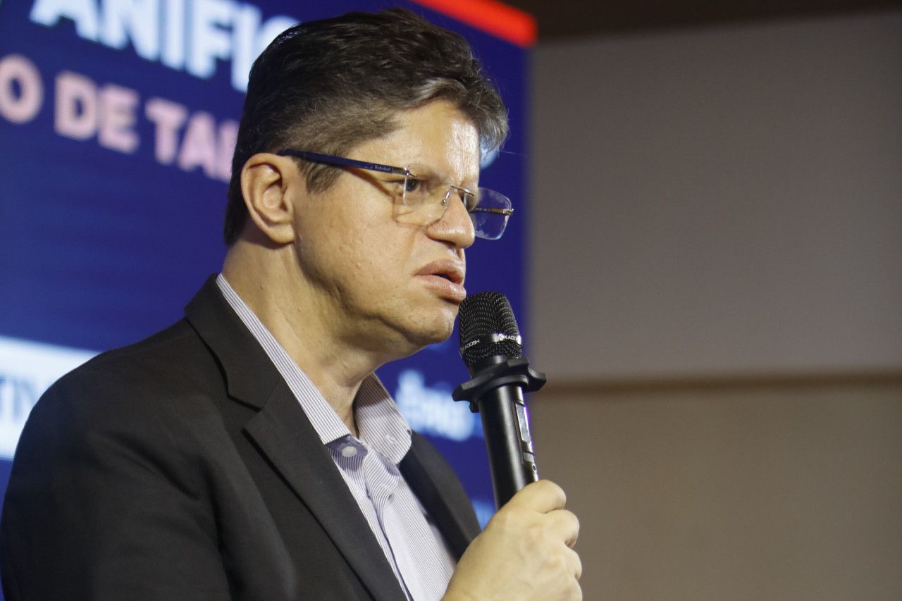 Um homem de terno e óculos está falando em um microfone.