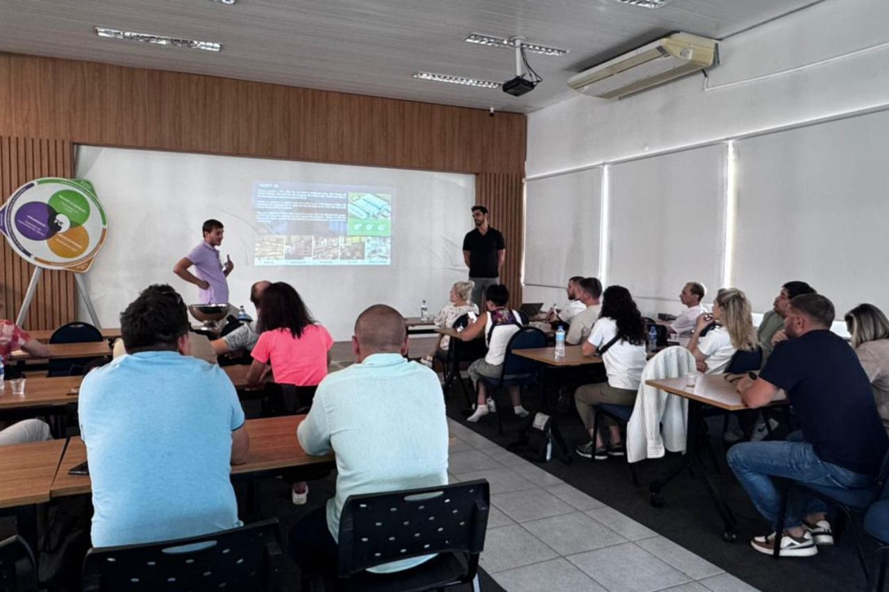 Um grupo de pessoas está sentado em mesas em uma sala assistindo a uma apresentação.