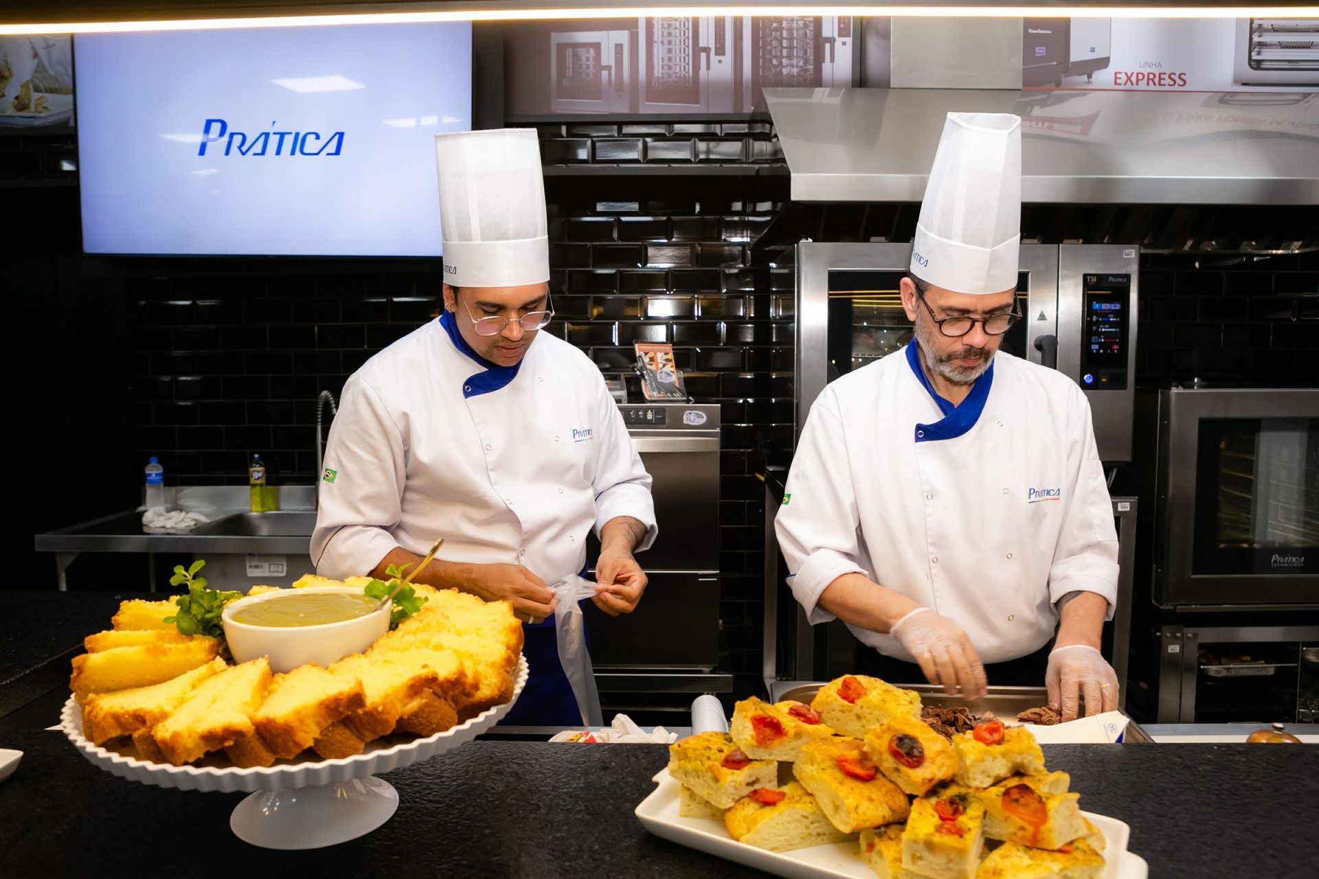 Dois chefs estão preparando comida em uma cozinha com uma placa que diz pratica