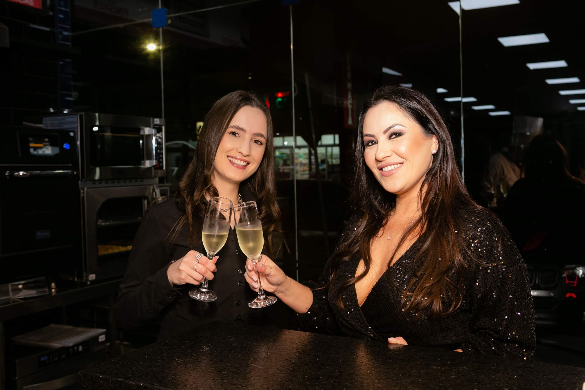 Duas mulheres estão sentadas em um bar segurando taças de champanhe.