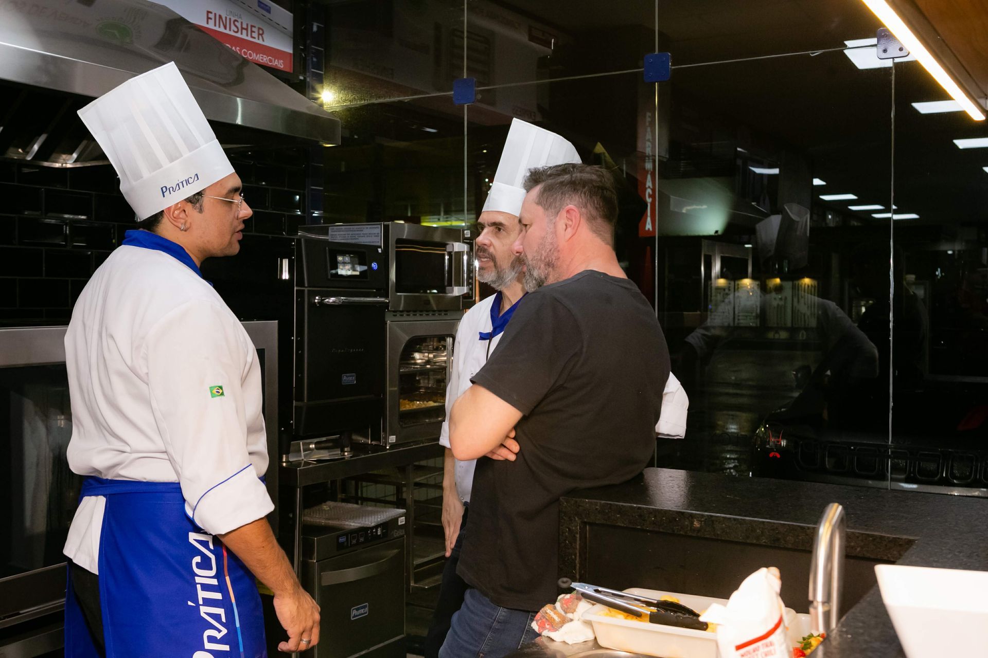 Um grupo de homens está em uma cozinha conversando entre si.