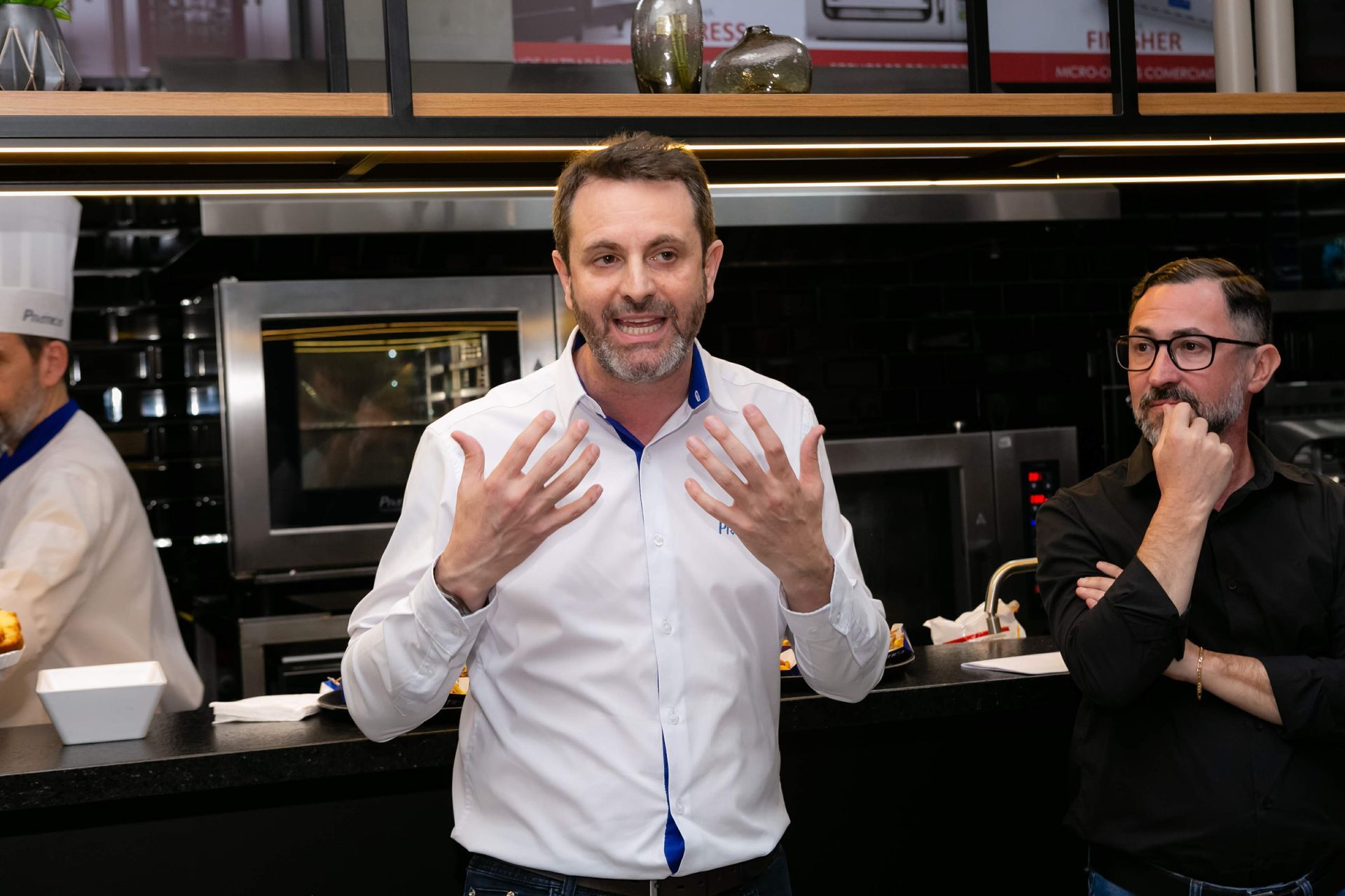 Um homem de camisa branca está conversando com outro homem na cozinha.
