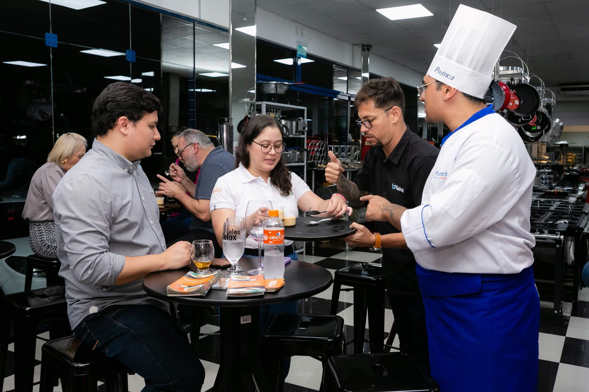 Um grupo de pessoas está sentado em mesas em um restaurante conversando com um chef.