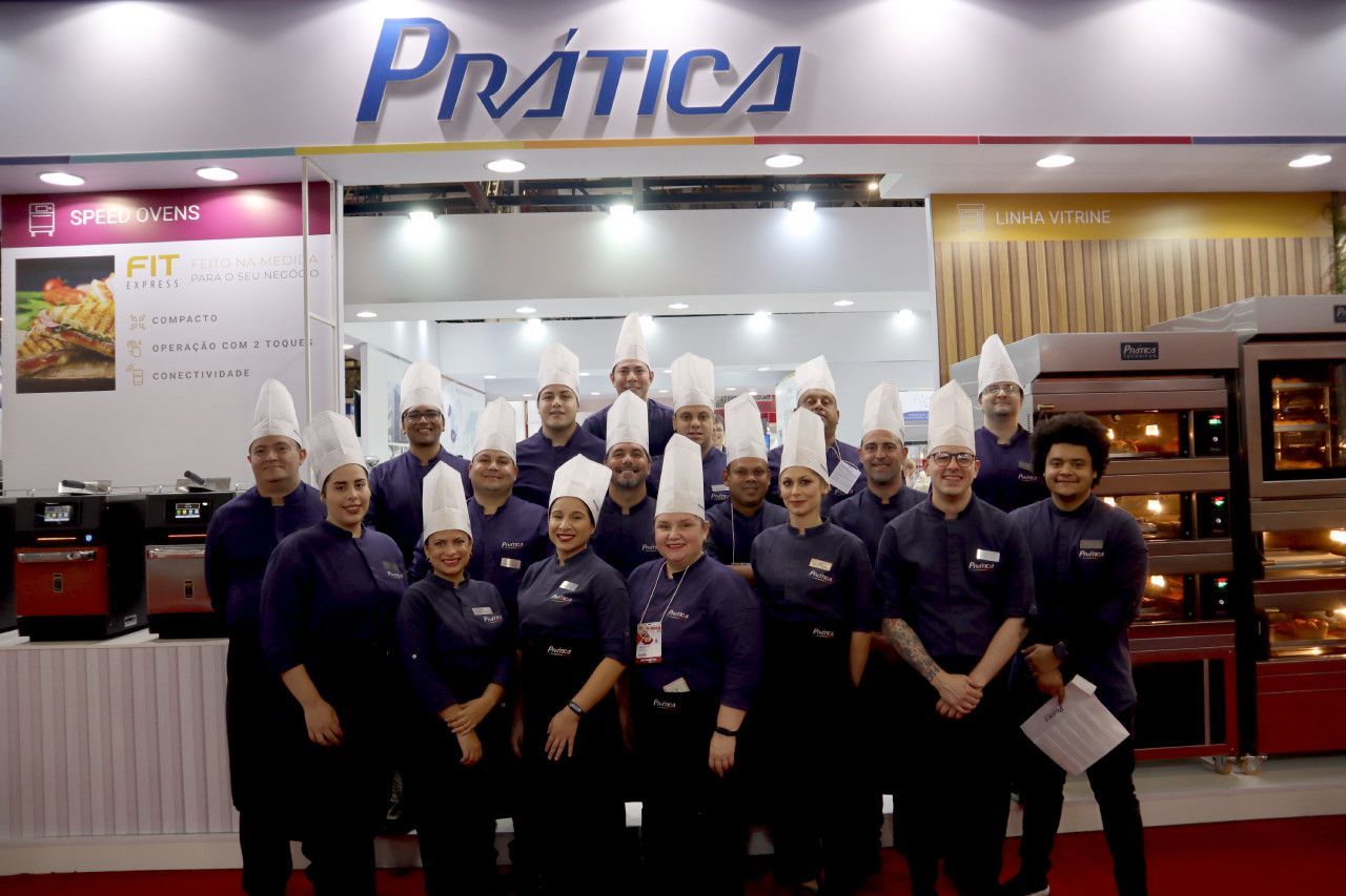 Um grupo de chefs está posando para uma foto em frente a uma placa de pratica.