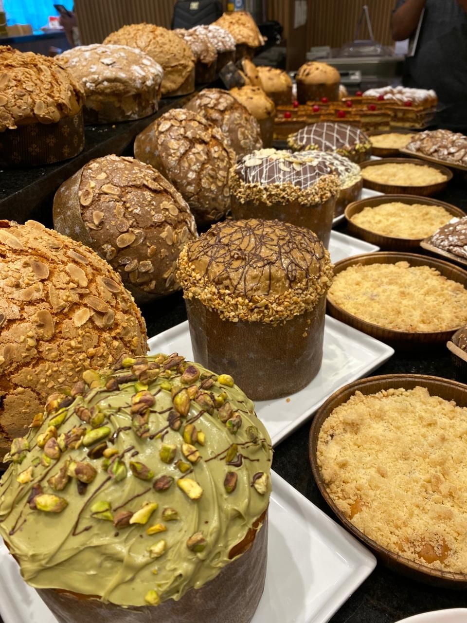 Exposição de diversos produtos de confeitaria decorados, incluindo bolos redondos, com coberturas como nozes e glacê.