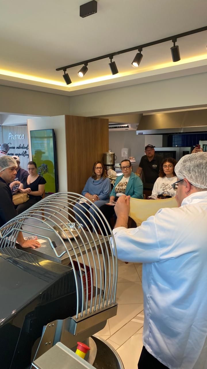 Padeiro demonstrando o uso da massa para um grupo em um ambiente de padaria.