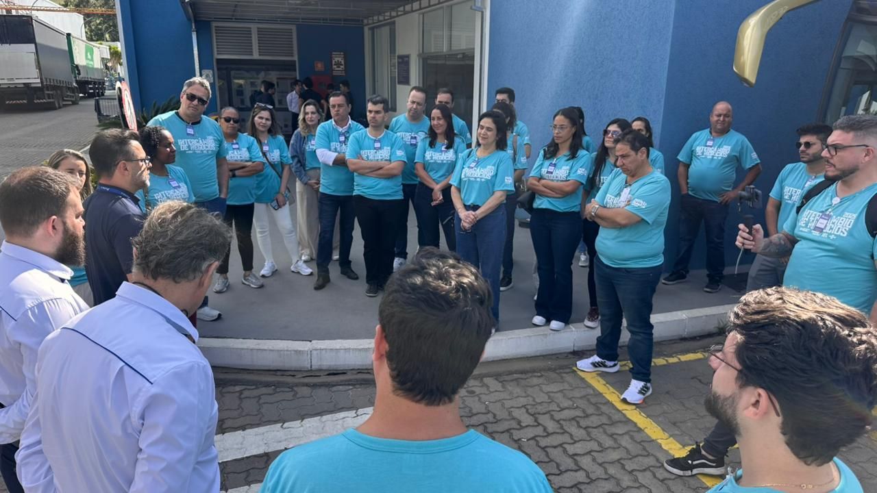 Grupo de pessoas vestindo camisas azuis em pé do lado de fora de um prédio, algumas com os braços cruzados.