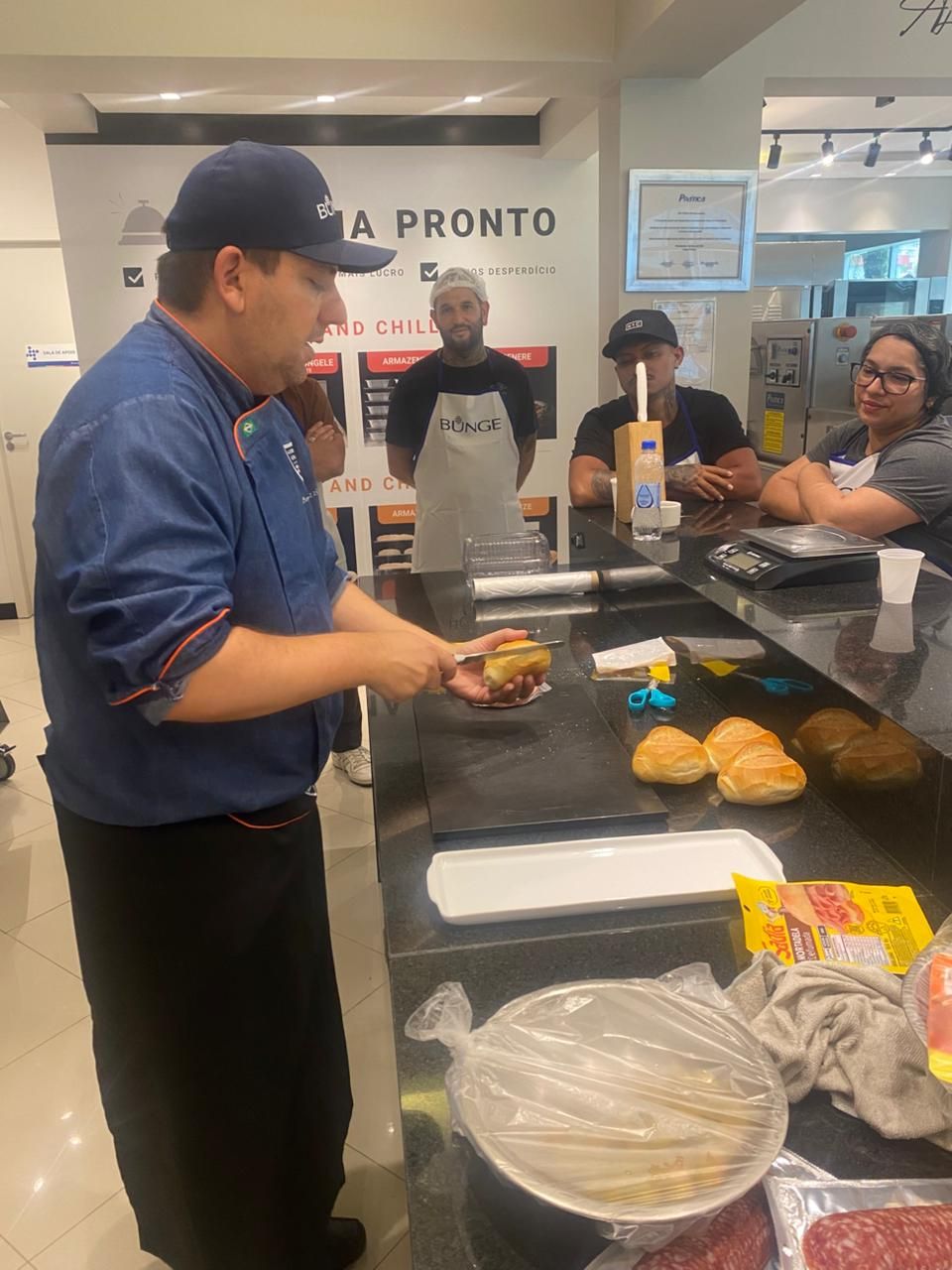 Chef preparando um hambúrguer durante uma demonstração culinária em uma cozinha.
