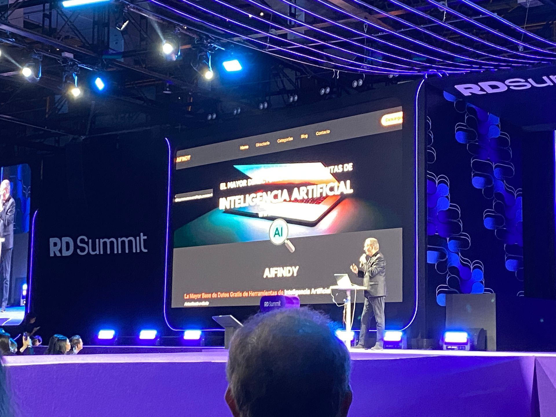 Um homem discursando no palco do RD Summit, com um grande telão atrás dele exibindo 