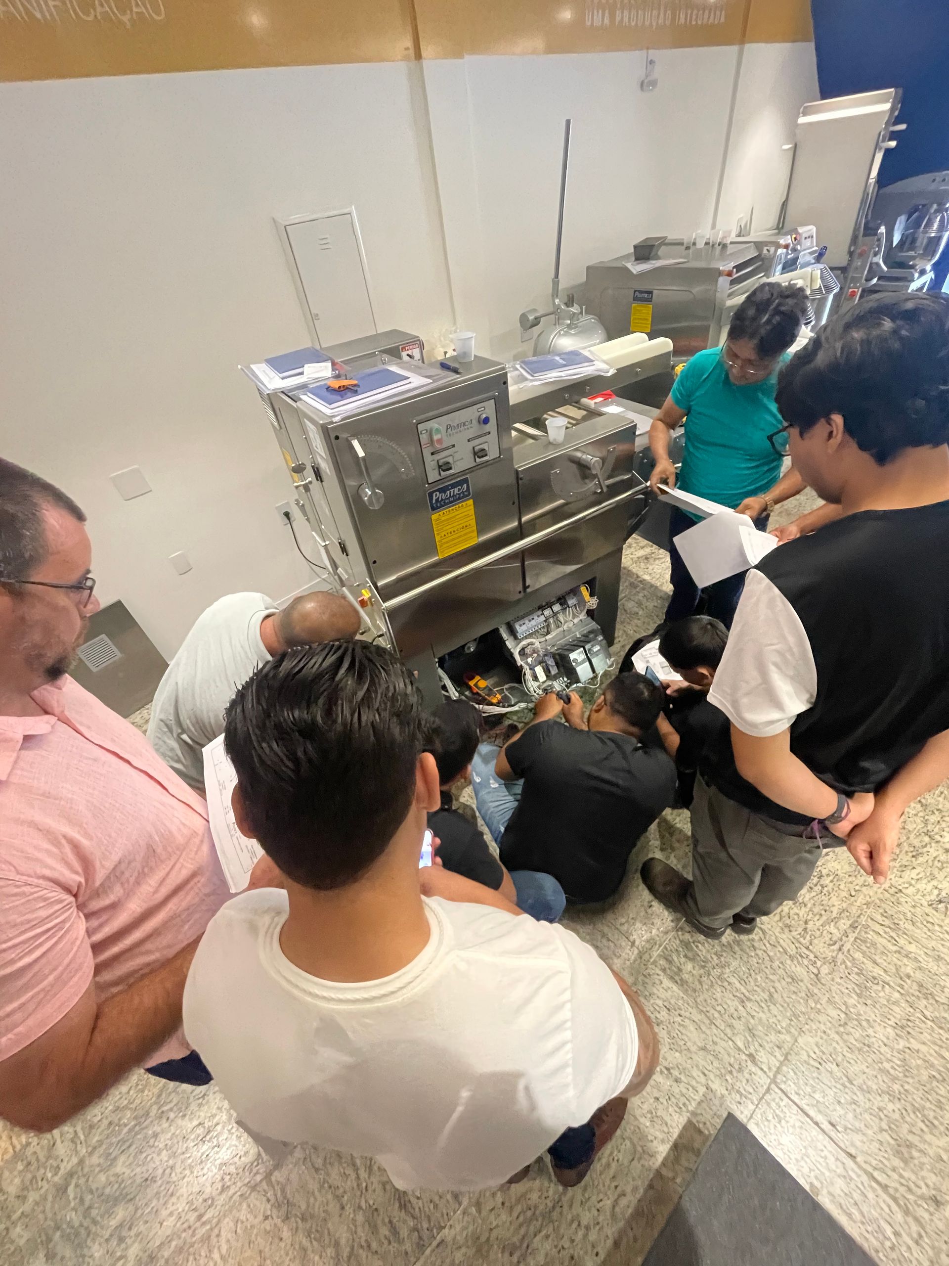 Um grupo de pessoas se reúne em torno de uma grande máquina industrial de aço