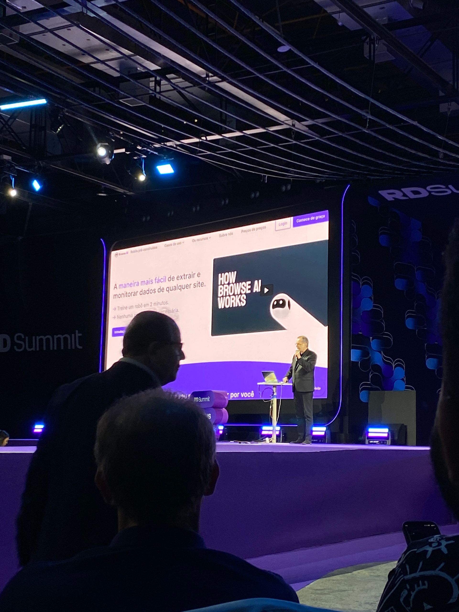 Homem apresentando em um palco durante uma conferência, com o texto 