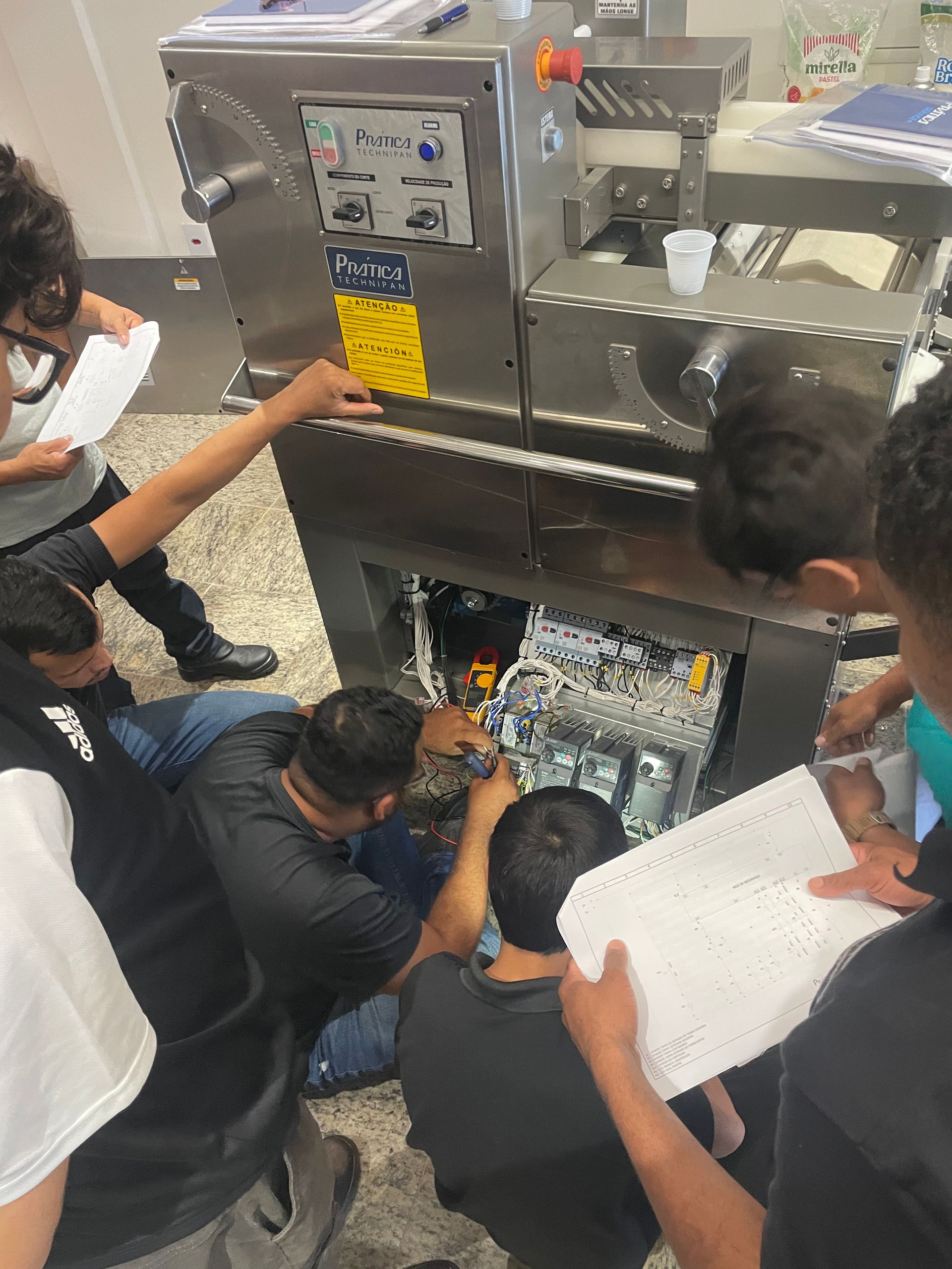 Um grupo de pessoas se reúne em volta de uma grande máquina de processamento de alimentos de aço inoxidável
