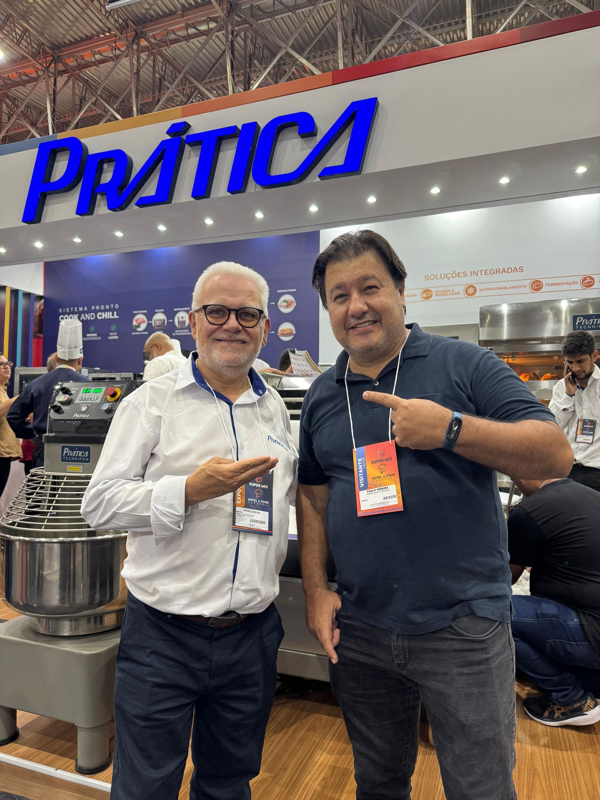 Dois homens posam em frente a uma placa com a palavra 