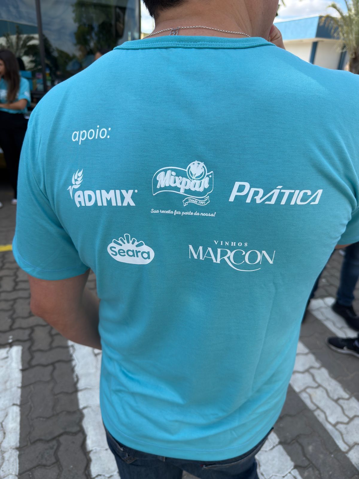 Costas de uma pessoa vestindo camisa azul com vários logotipos de empresas.