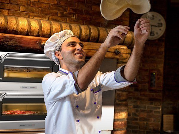 Um homem com uniforme de chef está jogando massa de pizza no ar.