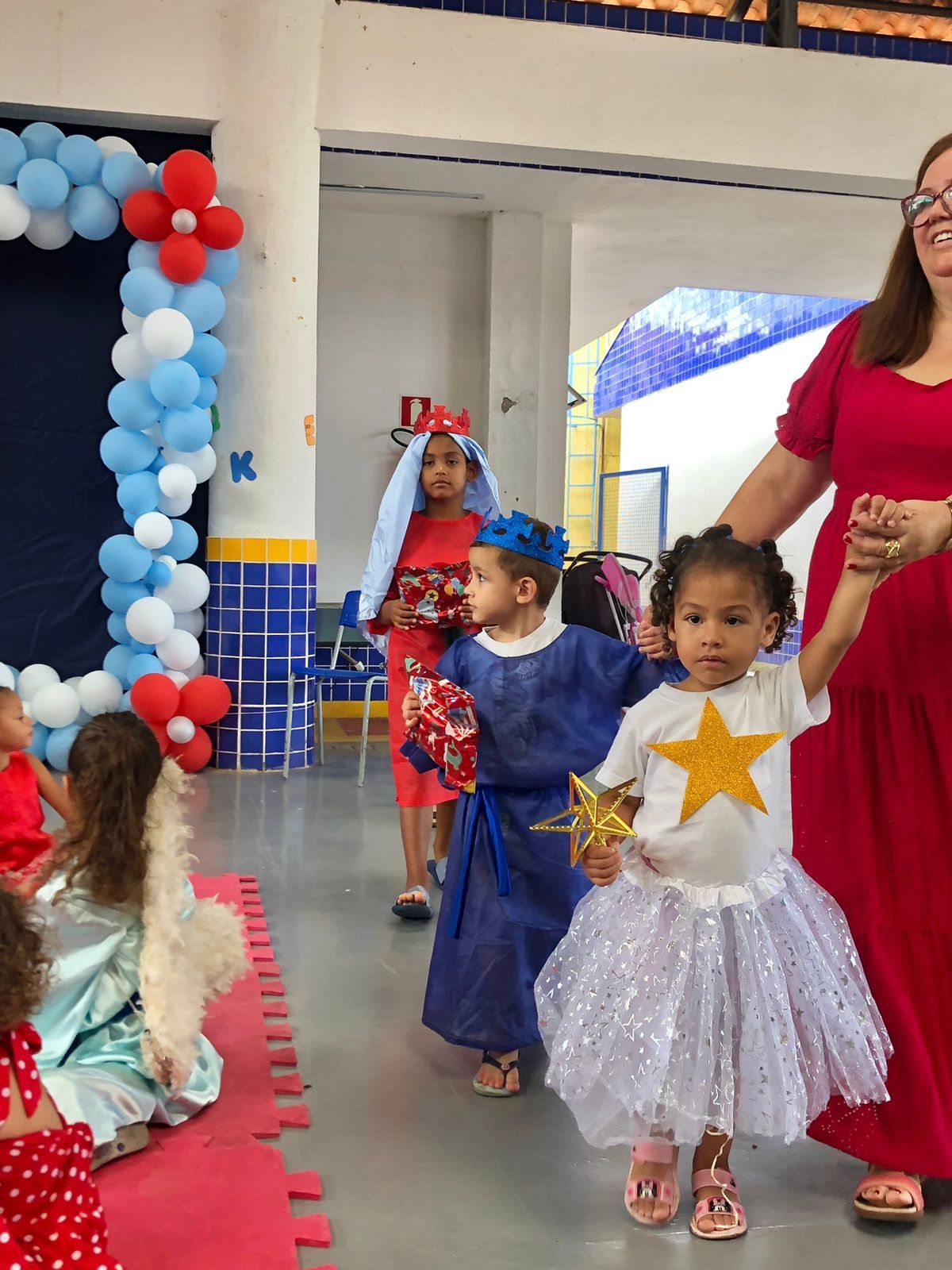 Uma mulher de vestido vermelho segura a mão de uma menina com uma estrela na blusa