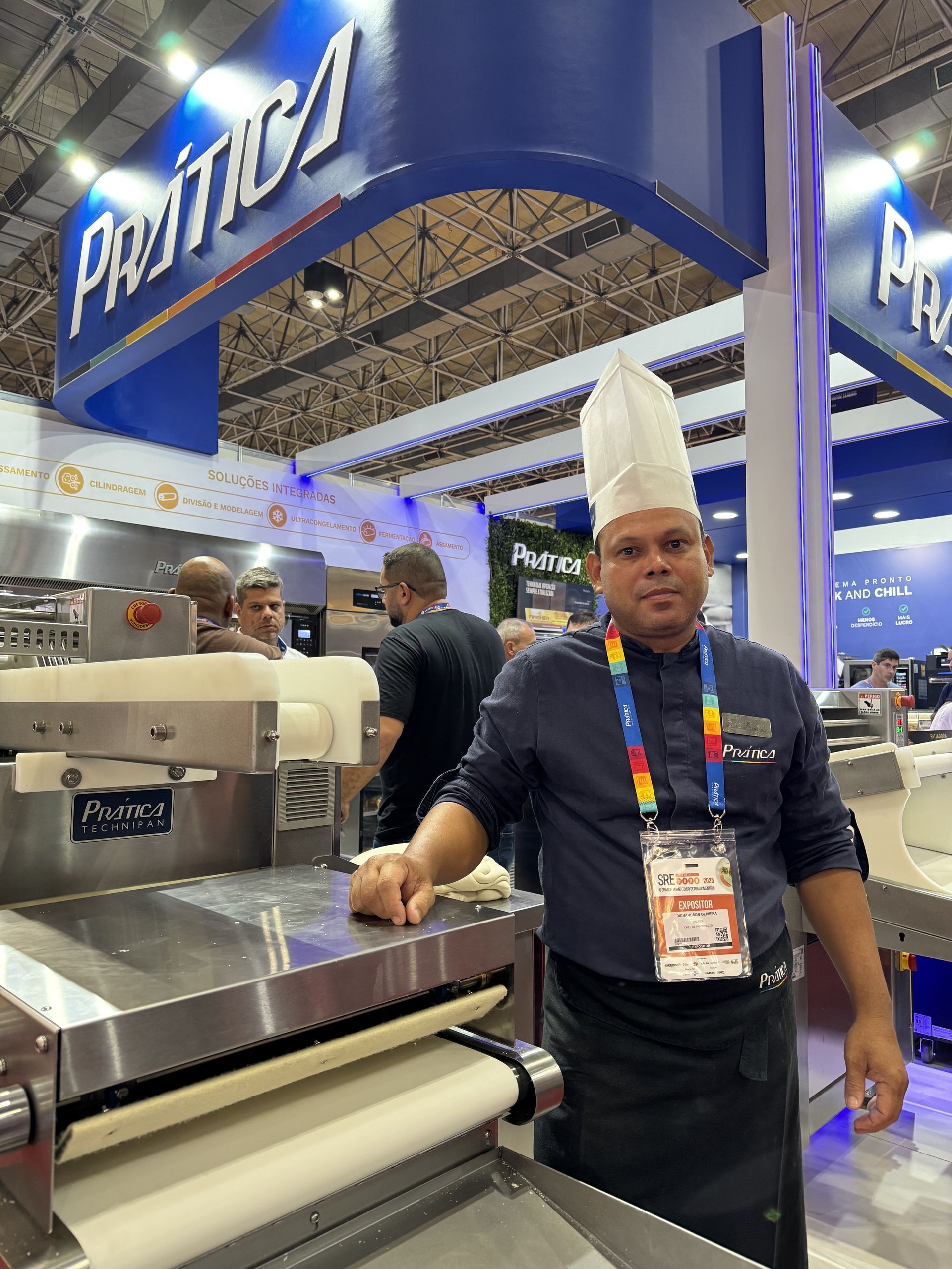 Um homem com chapéu de chef está parado em frente a uma máquina.