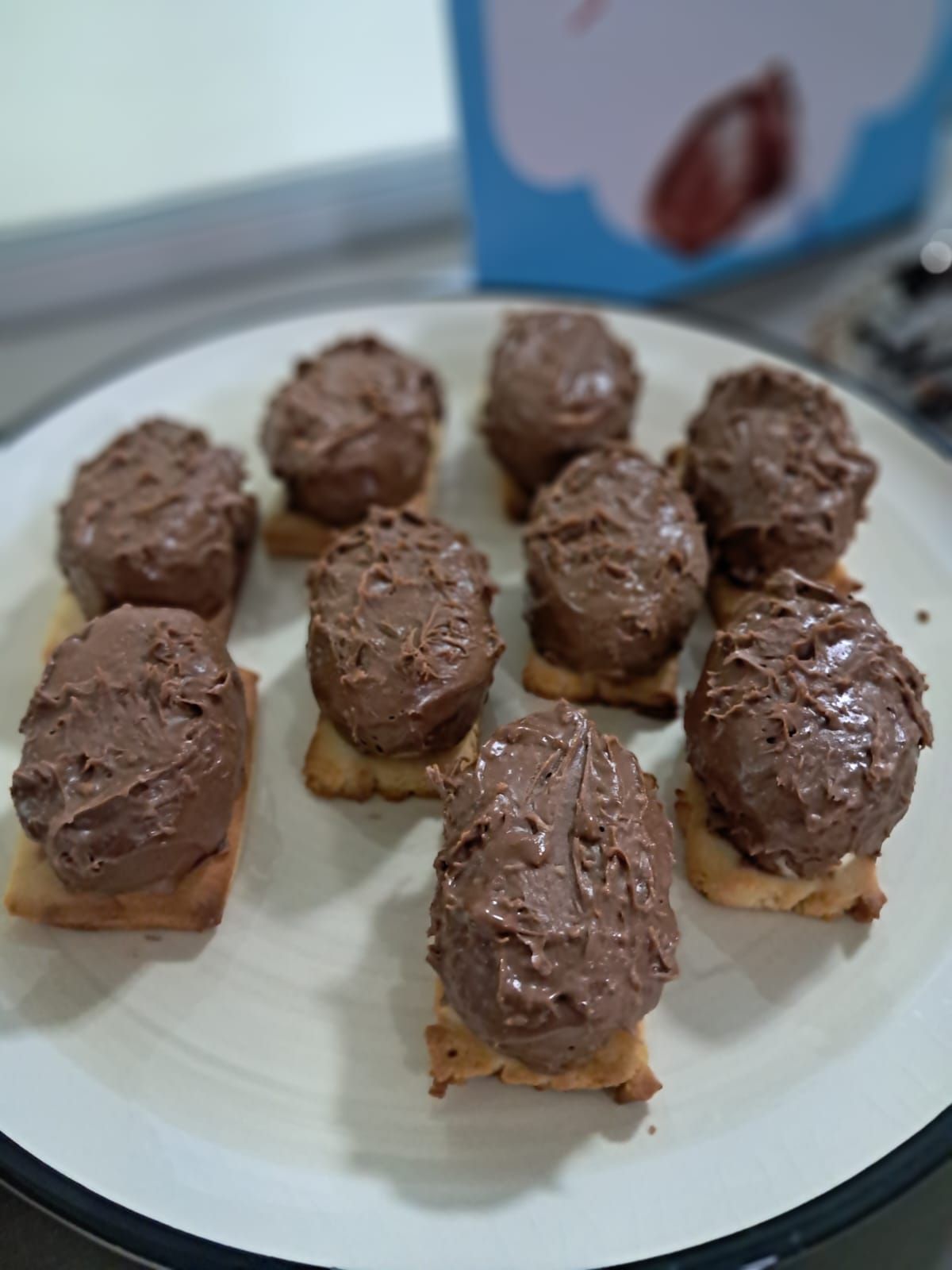Prato de guloseimas cobertas de chocolate, parecidas com mini ovos, sobre biscoitos quadrados.