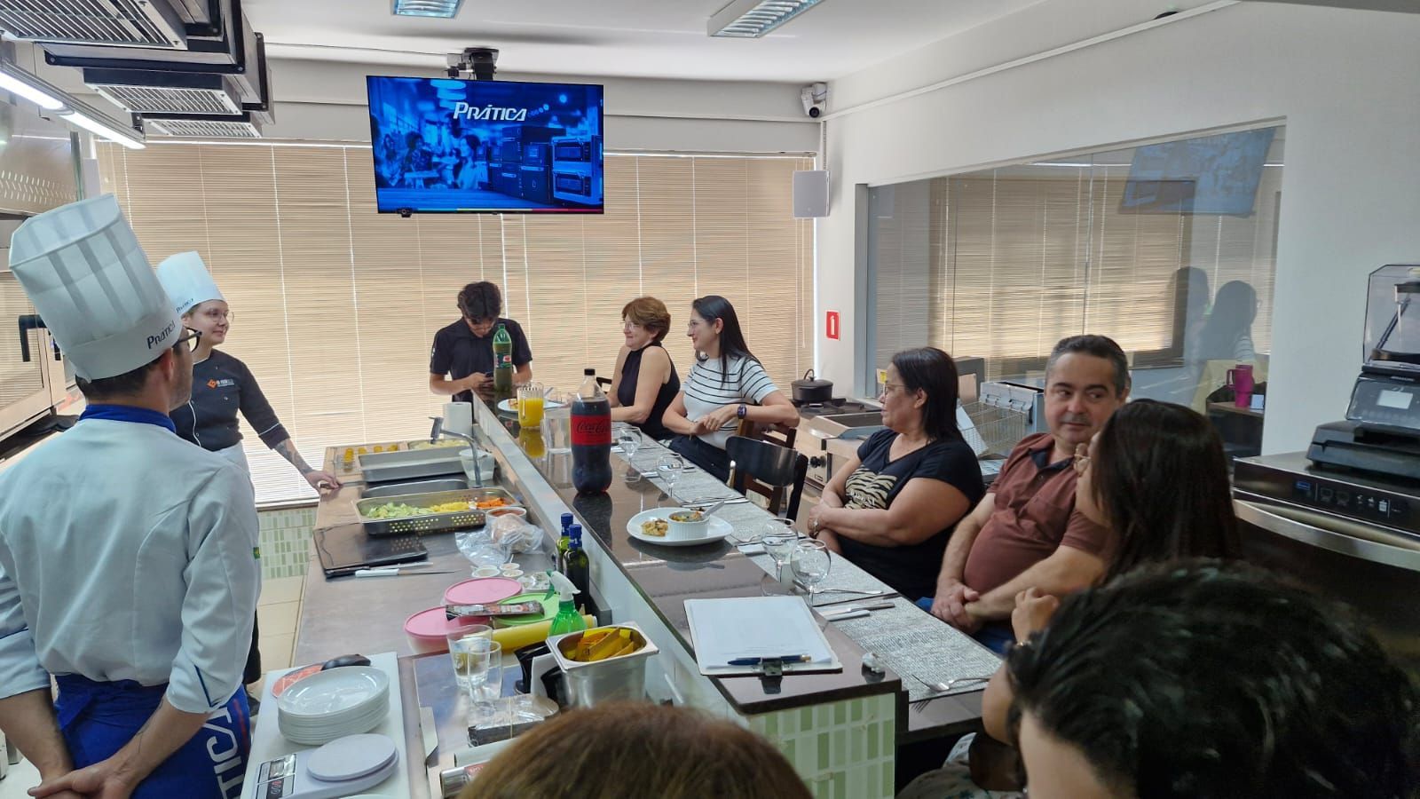 Um chef demonstra técnicas de culinária em um balcão para um pequeno público em uma cozinha.