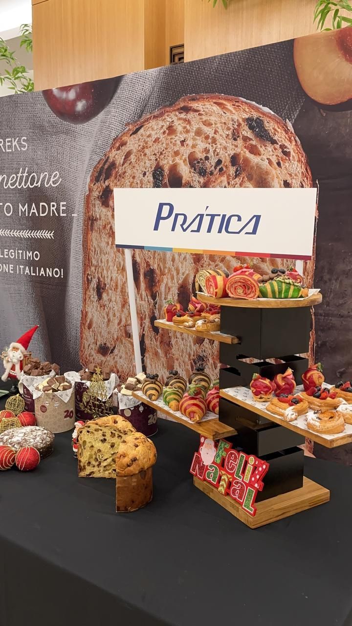 Exposição de produtos assados ​​sobre uma toalha de mesa preta; placa com os dizeres 