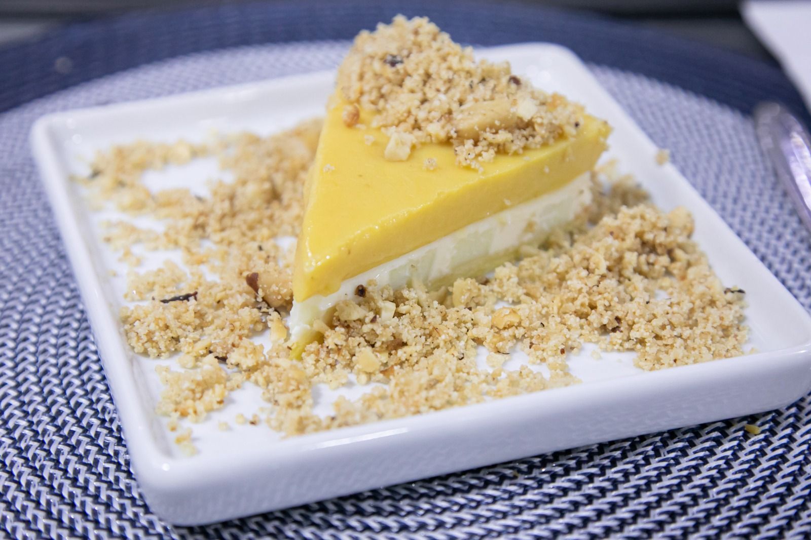 Fatia de cheesecake de manga em um prato branco, coberta com migalhas.