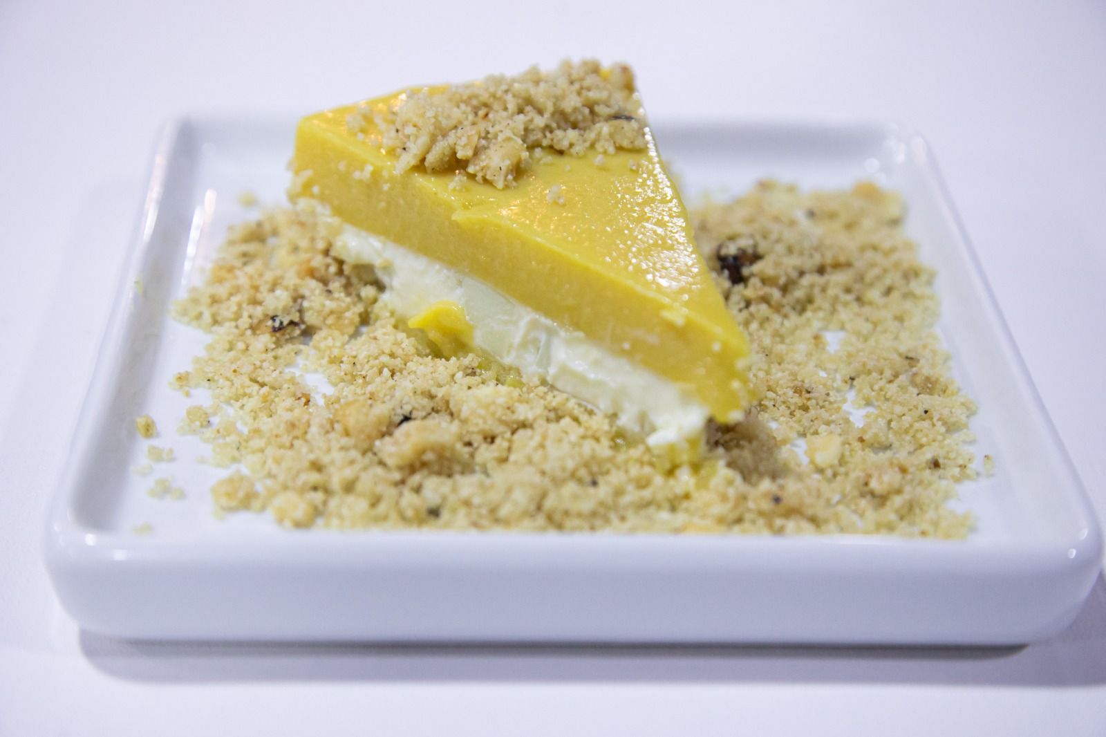 Fatia de sobremesa em camadas com cobertura amarela, base branca e crosta crocante em um prato branco.