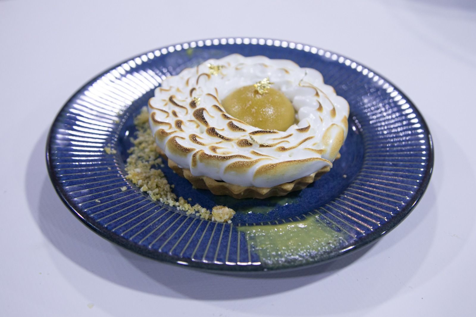 Tarte de limão com merengue flambado em prato azul.